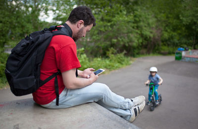 Side view of man using mobile phone while sitting on ledge