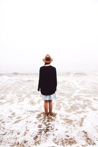 Rear view of woman standing with ankle deep in sea against sky