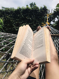 Cropped image of hand holding book against plants