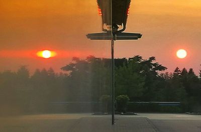 Road by trees against orange sky