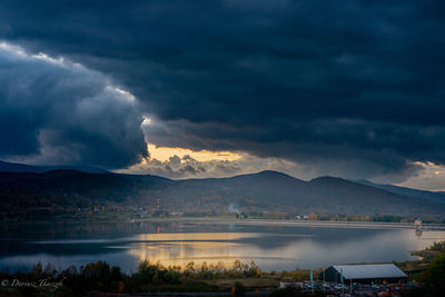 Scenic view of lake and mountains against storm clouds