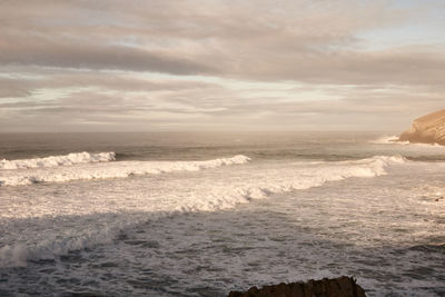 Waves rushing towards shore against sky