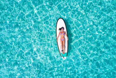 Aerial view of woman in bikini lying on surfboard over sea