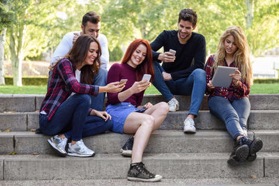 Friends using wireless technology while sitting on staircase