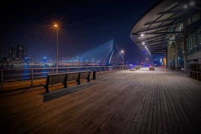 Empty promenade by river against erasmusbrug in city at night