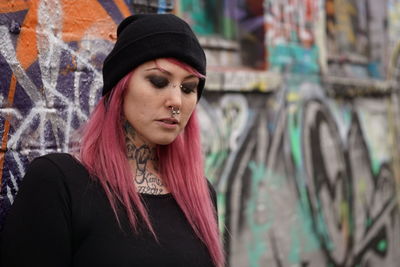 Young woman with pink hair standing against graffiti wall