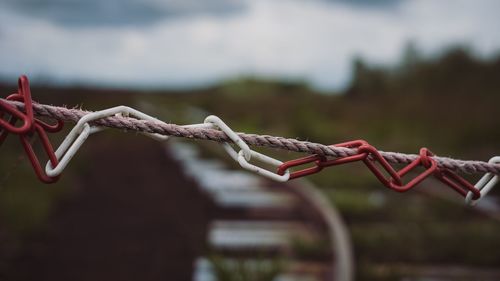 Close-up of chain hanging on rope against sky