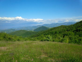 Scenic view of green landscape and mountains against blue sky