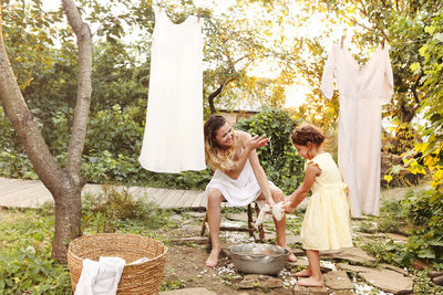 Full length of mother and daughter cleaning clothes outdoors