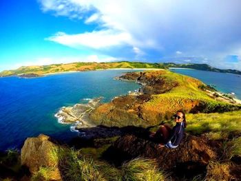 Woman sitting on cliff by sea against sky