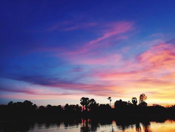 Silhouette trees by lake against sky during sunset