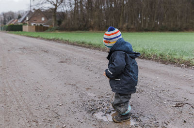 Side view of girl wearing warm clothing standing on dirt road