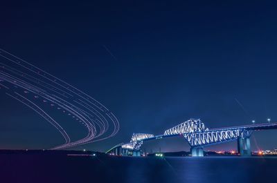 Illuminated bridge over river against sky at night