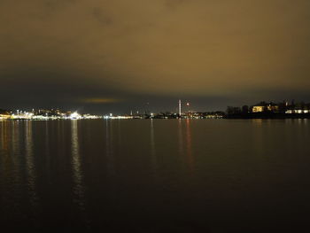 Illuminated cityscape by sea against sky at night