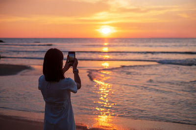 Woman photographing sea during sunset