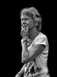 Senior woman looking away while standing against black background