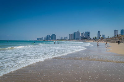 Scenic view of beach in city against clear blue sky