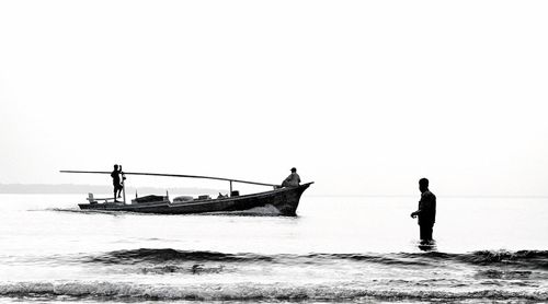 Silhouette man standing on fishing boat in sea against clear sky