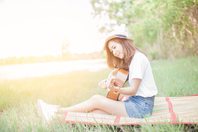 Young woman playing guitar on grassy field at park