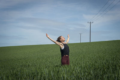 Woman standing in a field of wheat with her arms raised and enjoying the sun