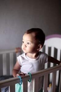 Cute boy looking away while standing in crib at home