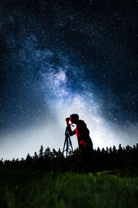 Silhouette man photographing on land against sky at night