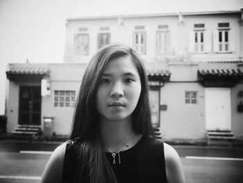 Portrait of young woman standing against building