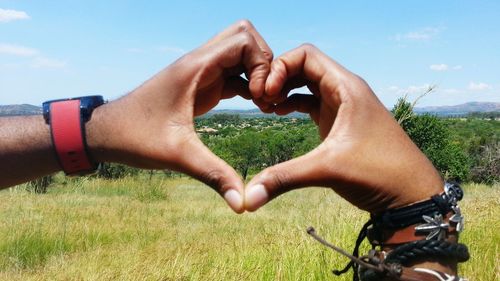 Cropped image of hands making heart shape against field