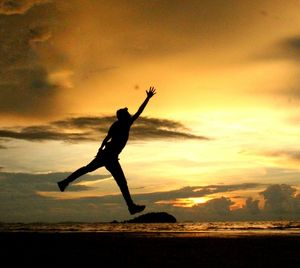 Silhouette man jumping in water at sunset