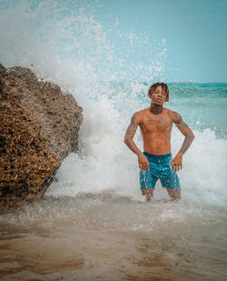 Portrait of shirtless man splashing water in sea