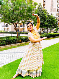 Portrait of smiling woman standing by plants, making a kathak pose