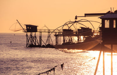 Silhouette fishing huts on sea against clear sky during sunset