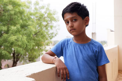 Portrait of boy standing by retaining wall in balcony