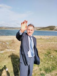 Portrait of businessman standing at riverbank against sky during sunny day