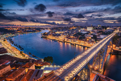 High angle view of illuminated city by river at sunset