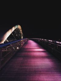 Illuminated footbridge against sky at night