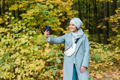 Young woman using phone while standing on plants