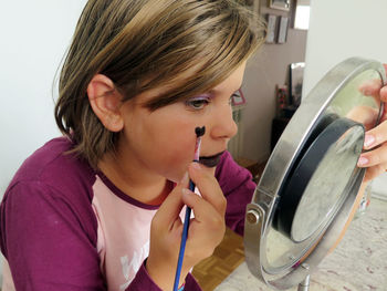 Close-up of girl applying make-up while looking into mirror at home