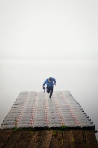 Man running on pier over sea against sky