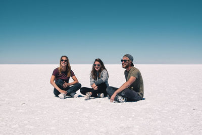 Young friends sitting on salt flat against clear sky