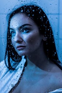 Close-up of young woman seen through wet glass