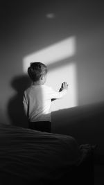 Rear view of boy touching wall in bedroom