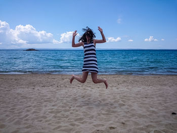Happy woman jumping at beach against sky