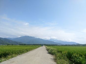 Empty road amidst field against sky