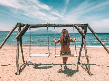 Rear view of woman sitting on swing against sea