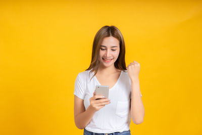 Young woman using mobile phone against yellow background