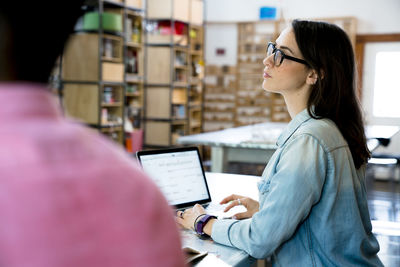 Businesswoman looking away while using laptop computer by male colleague