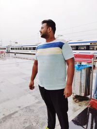 Young man looking away while standing against railing