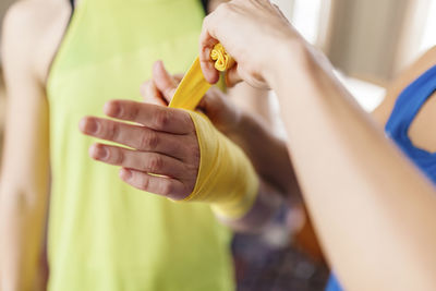 Cropped unrecognizable personal instructor helping fit female with wrapping hands with bandages for boxing while standing at home and preparing for training