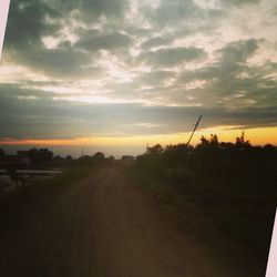 Road passing through field against cloudy sky